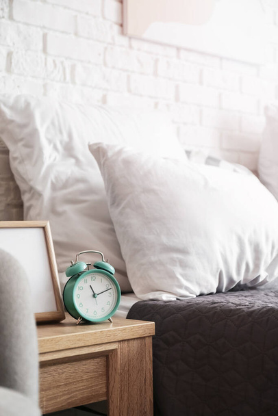 Alarm clock and frame on table in bedroom - Zdjęcie, obraz