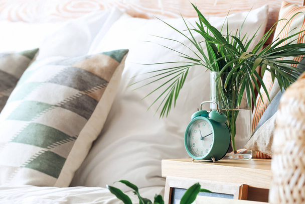 Relógio despertador e vaso com folhas de plantas na mesa de cabeceira - Foto, Imagem