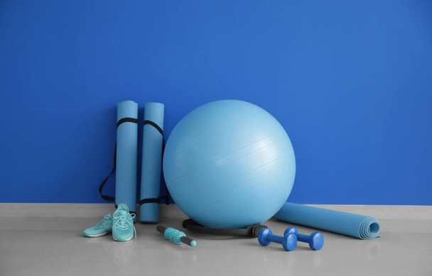 Set de equipamiento deportivo con balón de fitness y zapatos cerca de la pared de color - Foto, imagen