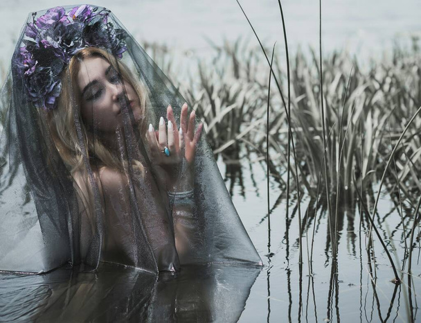 Beautiful girl in wreath of flowers at lake. Portrait of Young beautiful woman. Young pagan girl conduct ceremony on Midsummer. Earth Day - Photo, Image