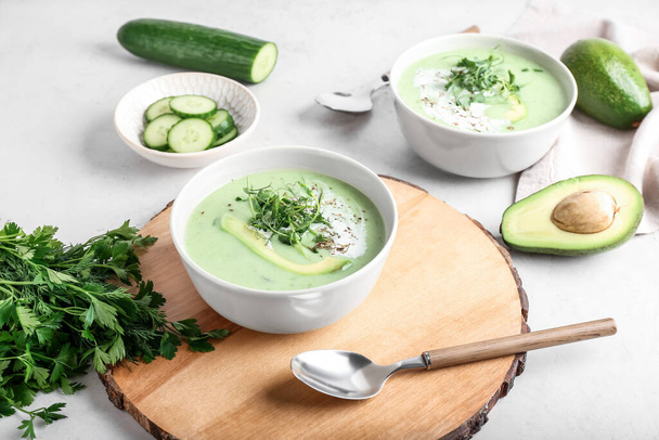 Schalen met groene gazpacho en ingrediënten op lichte achtergrond - Foto, afbeelding