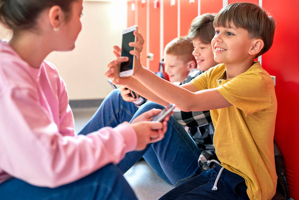 Schoolkinderen zitten op de vloer en gebruiken smartphone                                - Foto, afbeelding
