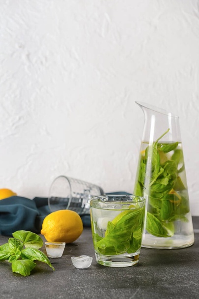 Glass and jug of lemonade with basil on light background - Foto, Imagen