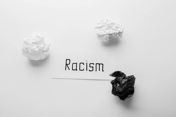 Χαρτί με λέξη RACISM και τσαλακωμένα χαρτιά σε λευκό φόντο - Φωτογραφία, εικόνα
