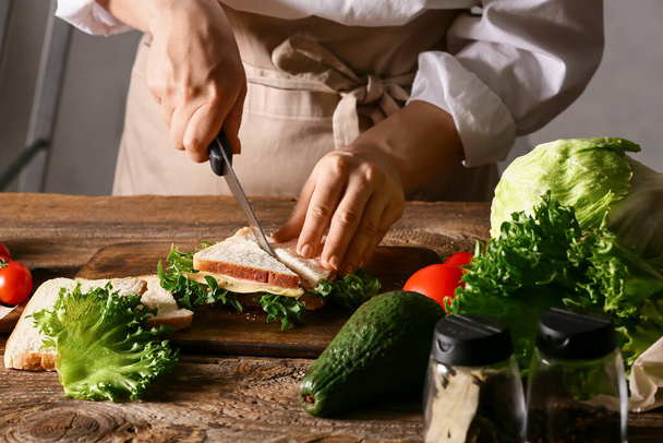 Frau schneidet leckeres Sandwich auf Holztisch - Foto, Bild