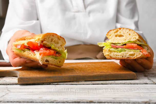 Женщина держит вкусные бутерброды на светлом деревянном фоне - Фото, изображение