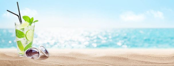 Playa de verano con arena caliente, hojas de palma y cóctel tropical. Concepto de vacaciones de viaje con espacio de copia - Foto, Imagen