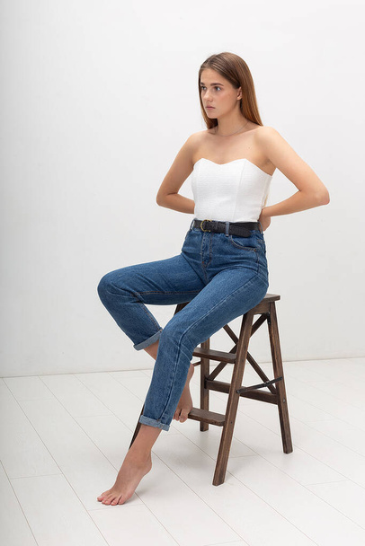 young caucasian woman with long brown hair in in corset, blue jeans at studio - Foto, Imagem
