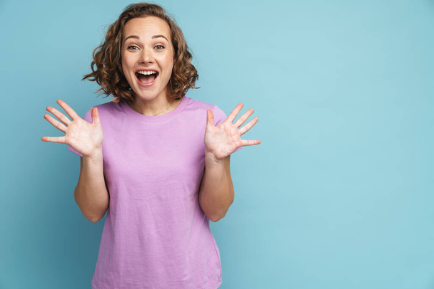Excited ginger woman with wavy hair gesturing and screaming at camera isolated over blue background - Foto, afbeelding
