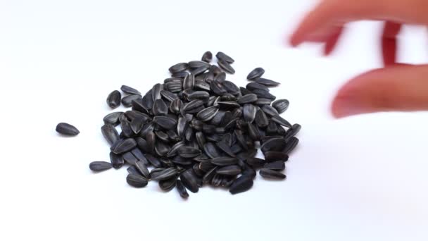 Ręka bierze czarne nasiona słonecznika na białym tle - Materiał filmowy, wideo