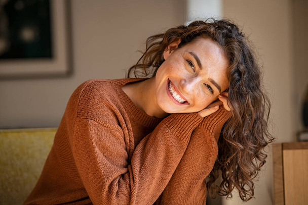 Happy young woman sitting on sofa at home and looking at camera. Portrait of comfortable woman in winter clothes relaxing on armchair. Portrait of beautiful girl smiling and relaxing during autumn. - Foto, immagini