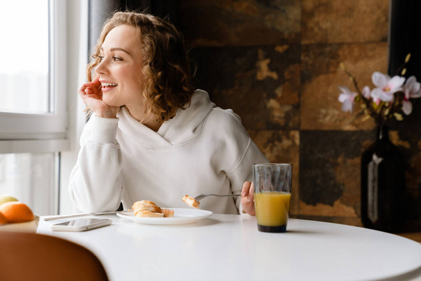 White blonde woman having breakfast while sitting at table in home - Foto, Bild