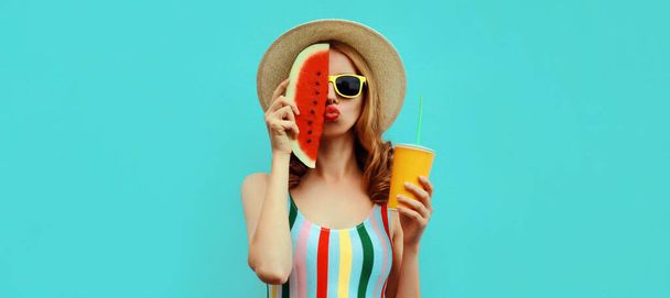 Letní barevný portrét krásné mladé ženy foukání její rty s plátek melounu a šálek šťávy nosí slaměný klobouk na modrém pozadí - Fotografie, Obrázek