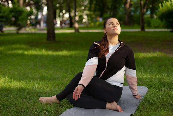 vrouw beoefent yoga in het park op groen gras. Pilates buiten. concept van geestelijke gezondheid - Foto, afbeelding