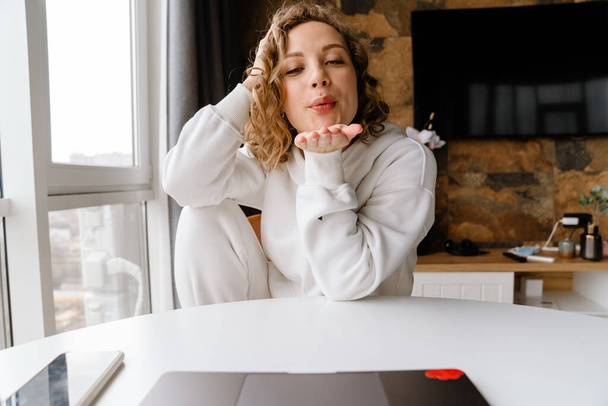 Young white woman blowing air kiss while using laptop at home - Fotoğraf, Görsel