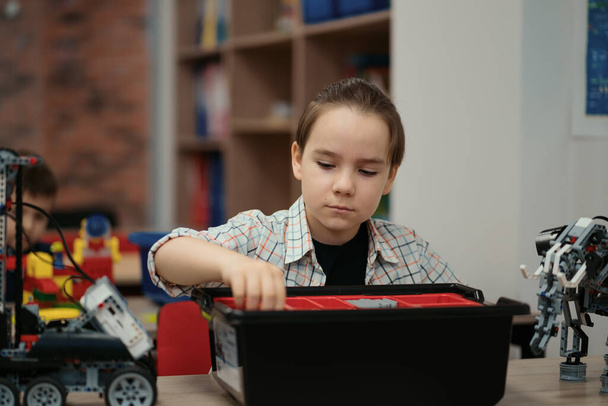 Chytrý školák sedí u stolu a staví robotické zařízení - Fotografie, Obrázek