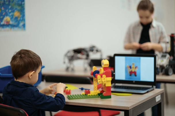 Dos niños niños de diferentes edades jugando con un juguete robot en la clase de robótica escolar - Foto, imagen