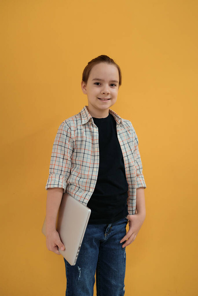 Smiling school boy holding a laptop on yellow wall background. - Photo, Image
