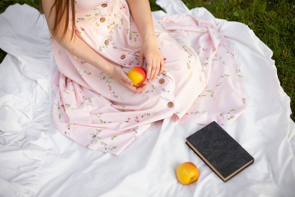 dívka v šatech sedí na podložce v parku a drží v rukou jablko - Fotografie, Obrázek