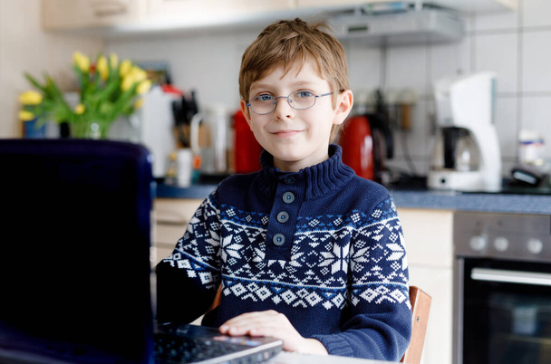 Gözlüklü çocuk evde okulda laptopta öğreniyor. Ev ödevi yapan, defter ve modern aletler kullanan sevimli bir çocuk. Evde eğitim kavramı. - Fotoğraf, Görsel