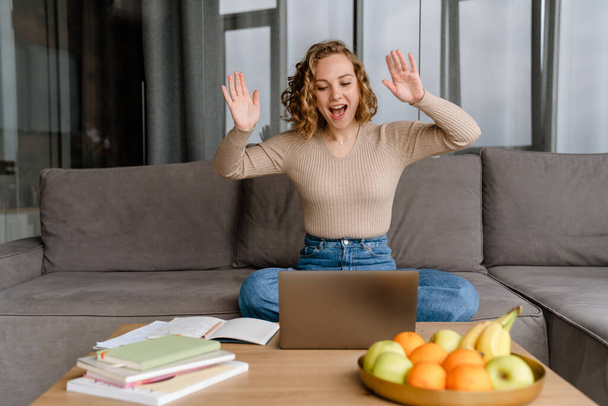Young white woman gesturing and using laptop while sitting on couch at home - Φωτογραφία, εικόνα