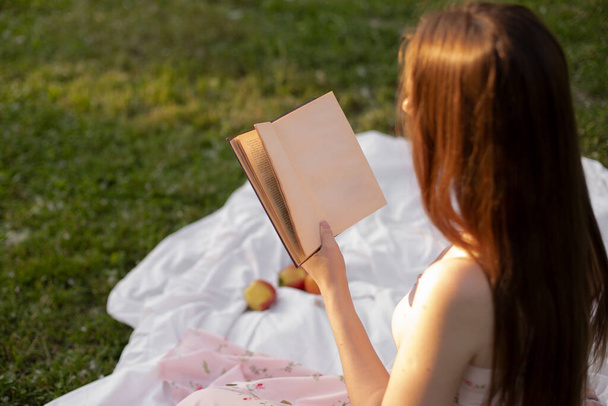 girl reading a book with a blank page sitting on the grass in the park. place for your design, mockup - Foto, afbeelding