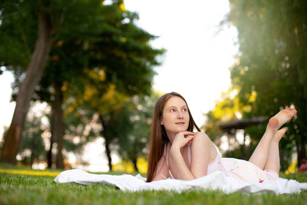 beautiful girl lies on green grass with a mat in the park, looking up thoughtfully - Photo, Image