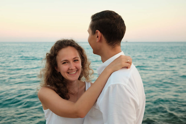 Woman embraces her beloved man smiling against seaside sunset - Fotó, kép