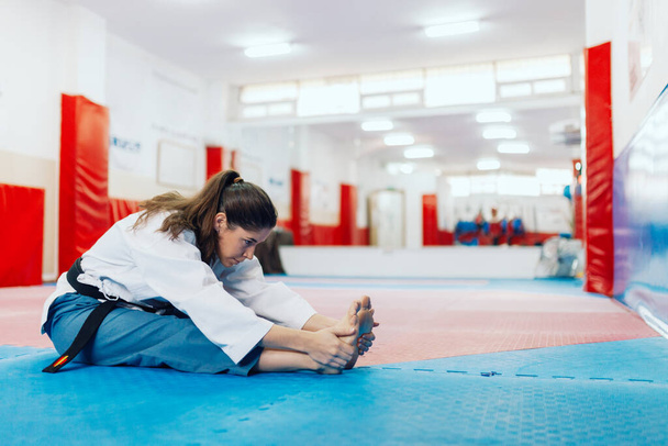 Młoda kobieta rozciągająca się w dojo w taekwondo dobok - Zdjęcie, obraz
