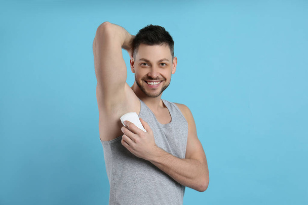Handsome man applying deodorant on turquoise background - Fotó, kép