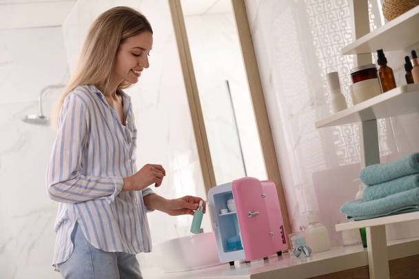 Woman taking cosmetic product from mini fridge in bathroom - Foto, Bild