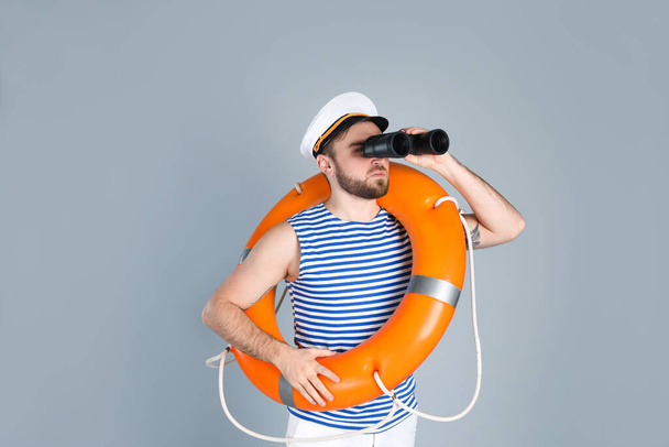 Sailor with binoculars and ring buoy on light grey background - Photo, image