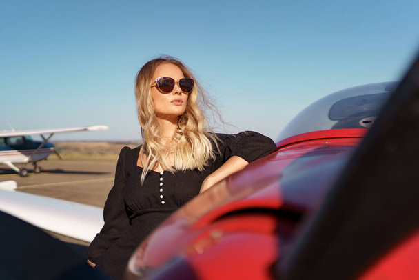 Preciosa dama en gafas de sol posando cerca de avión - Foto, Imagen