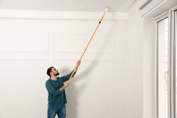 Young man painting ceiling with white dye indoors, space for text - Foto, Imagem