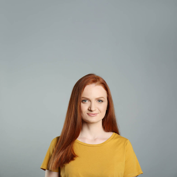 Candid portrait of happy young woman with charming smile and gorgeous red hair on grey background - Fotoğraf, Görsel