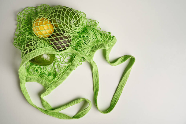 Green string eco shopping bag with vegatables avocado, lemon on grey background - Фото, зображення