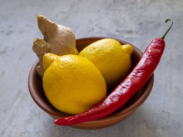 Vista lateral de limón amarillo, chile rojo y jengibre marrón en un plato de arcilla. - Foto, imagen
