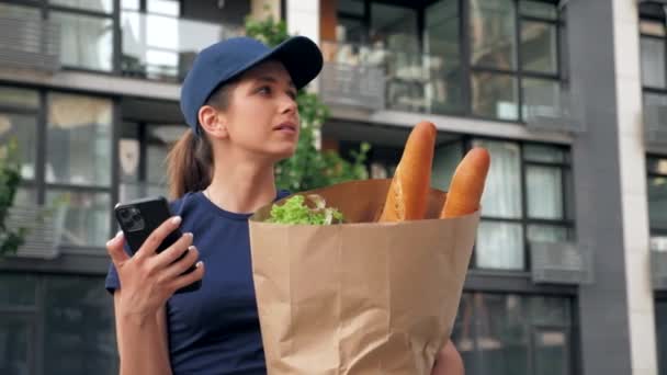Consegna cibo donna corriere utilizza smartphone tiene sacchetto di carta alla ricerca indirizzo - Filmati, video