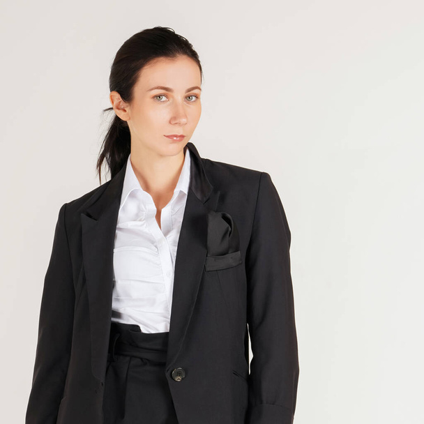 Νεαρή καυασιάτισσα επιχειρηματίας με λευκό πουκάμισο και μαύρο κοστούμι στέκεται σε μια σκηνή λευκής φωτογραφίας. Πορτρέτο σε λευκό φόντο με φως στούντιο. - Φωτογραφία, εικόνα
