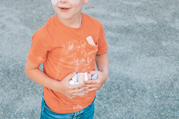 Niño sosteniendo tiza de color en sus manos y sucia camiseta en frente. Foto de alta calidad - Foto, imagen