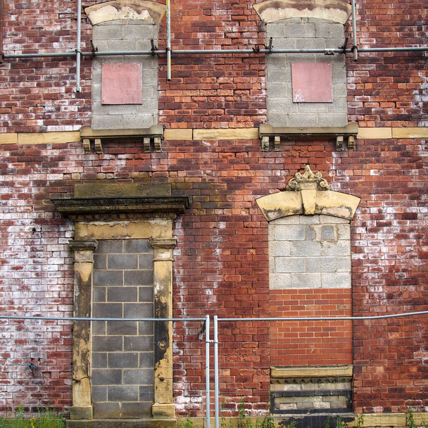 façade d'une vieille maison abandonnée avec des murs de briques en ruine et des fenêtres obstruées - Photo, image