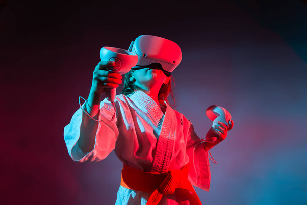 Young caucasian girl in karate uniform playing video games with virtual reality - Photo, Image