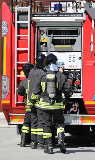 Teamwork van brandweerlieden en de rode brandweerwagen tijdens de noodsituatie - Foto, afbeelding