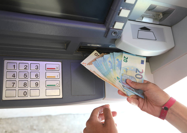 billetes en euros que acaban de retirarse del cajero automático y que la mano recoge con el teclado numérico tras introducir el PIN - Foto, imagen