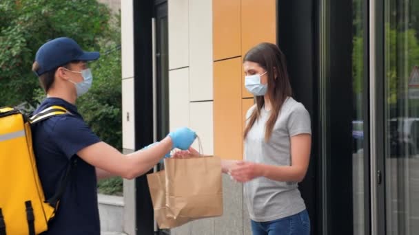 Dostawca nosi maskę i rękawiczki, aby dostarczyć zamówienie zamaskowany klient kobiety - Materiał filmowy, wideo