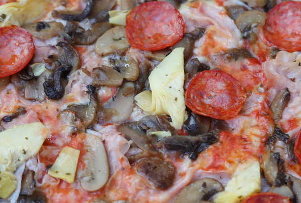 particolare della pizza chiamata capricciosa con funghi carciofi salame piccante e mozzarella di pomodoro in pizzeria - Foto, immagini
