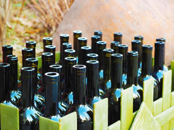 Plenty of empty wine bottles are in a green wooden box. Closeup photo - Photo, Image