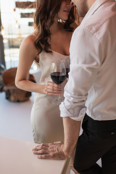 vista ritagliata di coppia in piedi e in possesso di bicchieri di vino rosso  - Foto, immagini