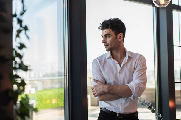 elegant man in white shirt standing with crossed arms near windows - Φωτογραφία, εικόνα