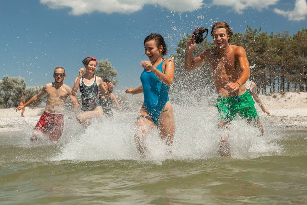 um grupo de amigos composto por homens e mulheres que correm na praia no mar - Foto, Imagem